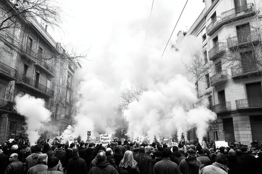 A crowd of people are standing in the street with smoke coming out of the buildings photo