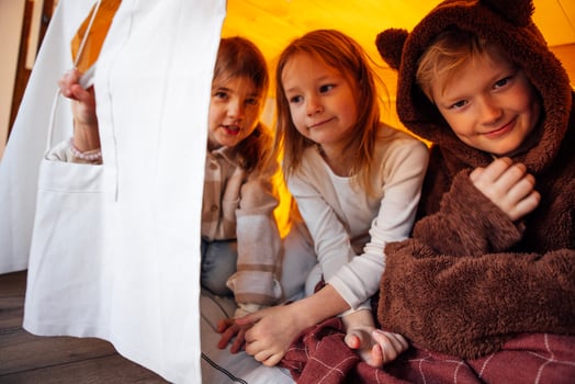 Small smiling children play in a tent at home. Friends are having fun and sitting under the table on a mattress in the living room. photo