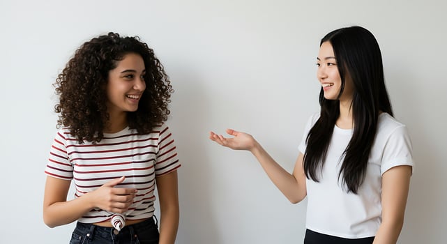 Two women talking to each other in front of a white wall photo