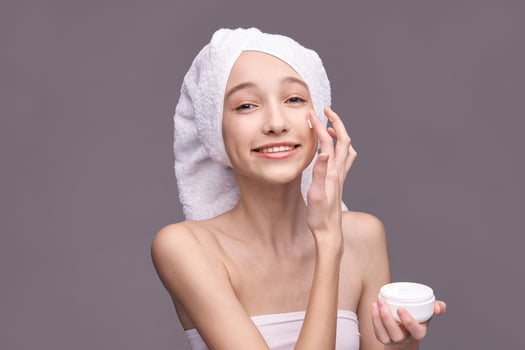Young caucasian female applying skincare cream with a towel on her head. photo