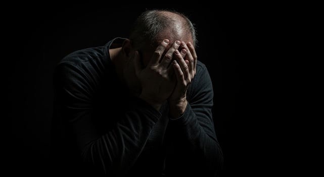 Depressed middle aged man covers his face with hands in dark studio photo
