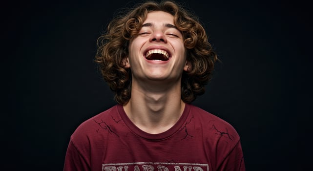 Young man with curly hair laughing joyfully eyes closed studio shot photo