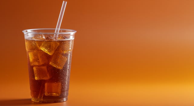 Refreshing cola beverage with ice cubes in a clear plastic cup on orange background photo