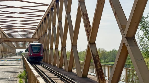 Red train glides through iron lattice, echoing nostalgic transit dreams, bridging Arbor Day serenity and Railroad Enthusiasts Month photo