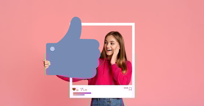 A young woman wearing a bright pink sweater looks excited while holding a large thumbs up symbol. This cheerful moment captures her joy in engaging with social media and her followers. photo