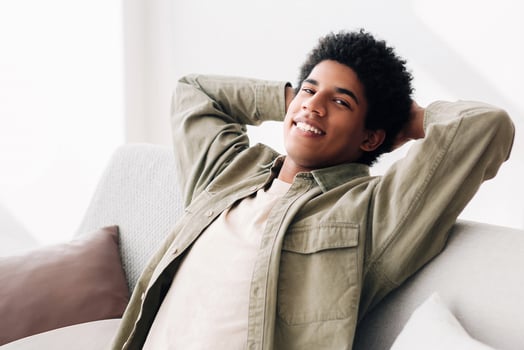 Peaceful black teenager resting on comfy couch at home during covid-19 lockdown, panorama. Happy African American teen guy relaxing on cozy sofa, being lazy on weekend morning photo