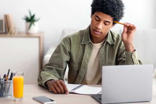 Thoughtful black teen guy passing hard exam or online test on laptop at home, panorama. Teenage male student learning remotely, doing difficult home assignment, working on educational project photo