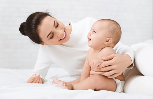 Happy childhood, Adorable baby laughing with mother, sitting on bed together photo