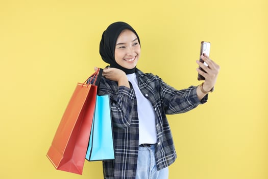 Cheerful Beautiful Asian Woman in Blue Shirt and Black Hijab Holding Shopping Bags photo