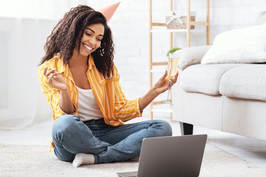 Virtual Party. Happy african american woman in hat having conference online meeting with friends and family, holding glass of wine, toasting and celebrating birthday, staying at home photo
