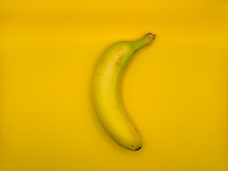 Bright yellow banana on yellow background in the center of the image, top view photo