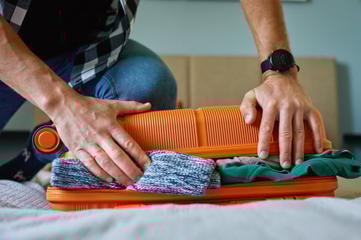 Man presses down on an overfilled orange suitcase while packing clothes. Male traveler has trouble while preparing for travel photo