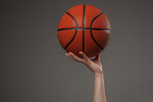 Close up of a woman hand confidently holding a basketball high against a dark background, symbolizing strength, sports, and empowerment in a minimalist composition. photo