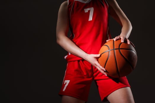 Female basketball player in red uniform holding ball confidently against dark background, symbolizing determination, athleticism, and focus before the game. photo