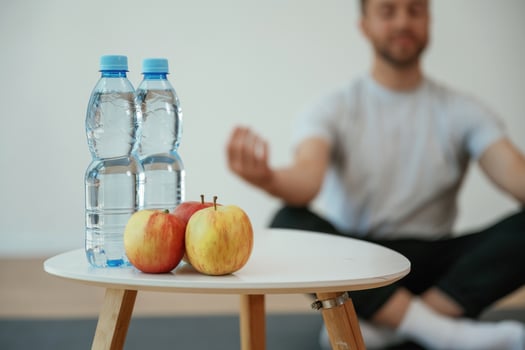 Focused view on apples and bottles of water. Yoga man is sitting on a mat at home photo