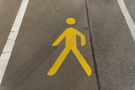 Bright yellow pedestrian symbol on asphalt indicates safe walking path near urban street during sunny day photo