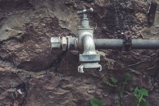 Water faucet emerges from rocky wall showcasing rustic charm in a forgotten outdoor space at twilight photo