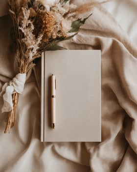 A notebook and pen on a bed with a bouquet of dried flowers photo