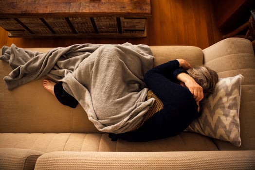 An elderly woman lies covered with a blanket and suffers from a headache at home. A mature lady sleeps on the couch and hugs herself by the shoulders. Top view. photo