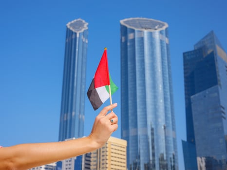 female hand holding tiny flag of UAE over city center photo