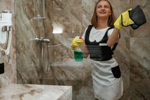 Green washing ,product, cleaning the glass in bathroom. Young chambermaid is in hotel room photo