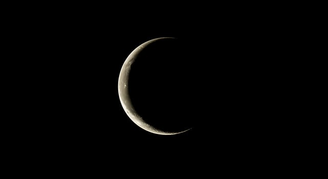 A crescent moon is seen in the dark sky photo