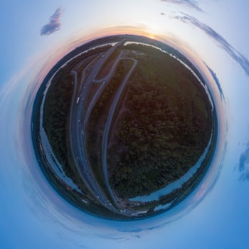 Creative aerial tiny planet panorama showing a highway on Barnaul city, green forest, and river under a colorful sunset sky. photo