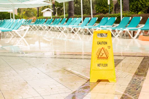 Warning sign caution wet floor among pool deck chairs near the hotel swimming pool photo