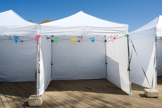 White Empty Folding Tents for Commercial Retail Shop with Colorful Bunting Flags on Wooden Deck. Vacant Place is Ready for Local Farmer at City Market, Waiting for New Goods photo