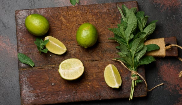 Bunch of fresh green mint and lime wedges on wooden board, top view. Cocktail ingredients photo