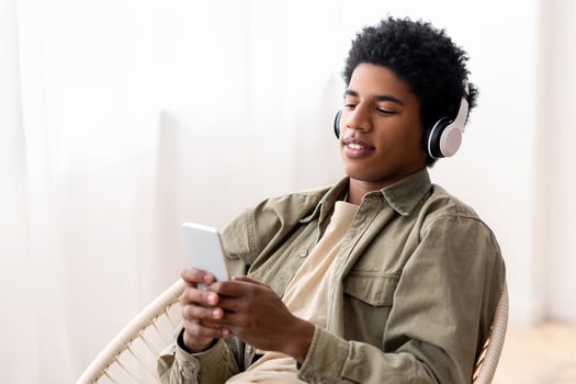 Handsome black teen in headphones choosing musical playlist on smartphone at home. Attractive African American guy enjoying great song, listening to audiobook or radio, indoors photo