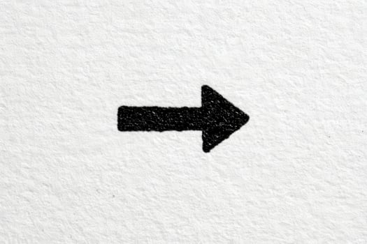A bold black arrow is drawn on a textured white paper, clearly indicating a rightward direction. The contrast between the black ink and white background highlights the arrows shape and intention. photo