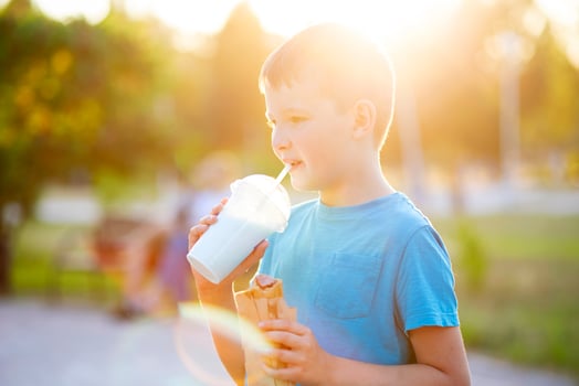Child boy eats hot-dog sandwich and drinks milkshake the park at sunset outdoors photo