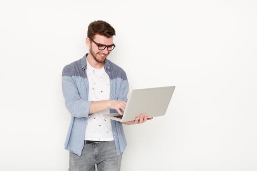 Young man standing with laptop. Handsome guy in glasses holding open notebook in his hand and work on it. Information, technology concept photo