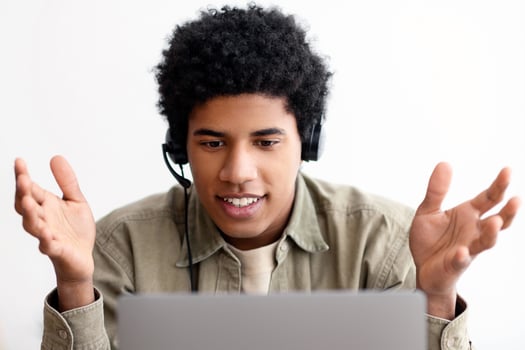 Web based education concept. Happy black teen student in headset talking to his college tutor online on laptop, indoors. Handsome teenager taking part in web conference or internet lesson from home photo