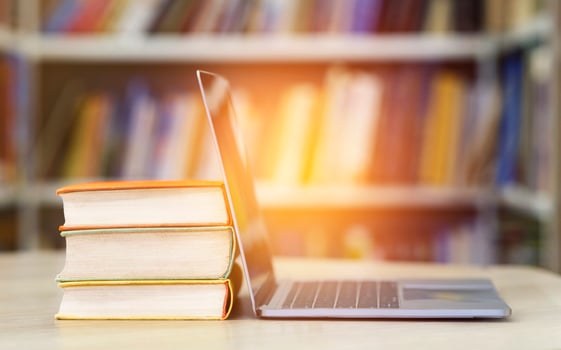 Digital Education And E-learning. Open laptop and stack of old books in blur school library or classroom background photo