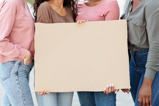 Four young ladies holding blank banner and looking at camera during women march. International group of female demonstrating outdoors with placards, women rights, feminism concept photo