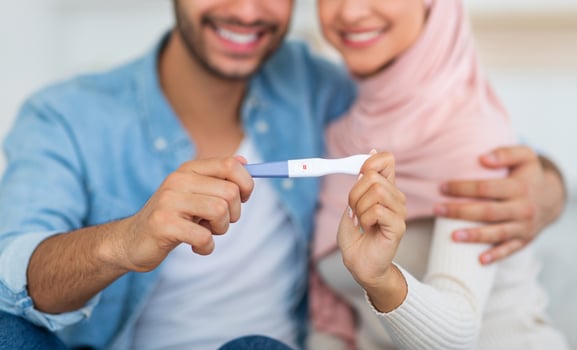 Muslim woman showing positive pregnancy test to camera, cuddling with her husband, selective focus. We are going to be parents. Childbirth and family life moments photo