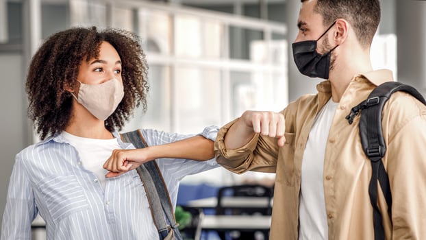 Touching elbows to say hello and social distance during covid-19 pandemic. Young man and african american woman greeting at work in morning in coworking office interior, empty space photo