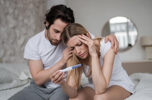 Upset young husband comforting his depressed young wife with negative pregnancy test on bed at home. Millennial couple cannot have baby, suffering from infertility indoors photo