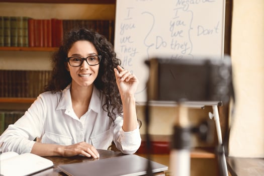 Online Lesson. Young female English language professor in glasses sitting at desk, teaching grammar rules, giving remote lecture. Woman recording blog for her internet channel using camera photo