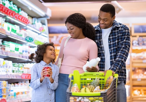 Family shopping concept. Young black parents with pretty daughter selecting food at supermarket. Cheerful black girl with mom and dad buying products at dairy department of big mall photo