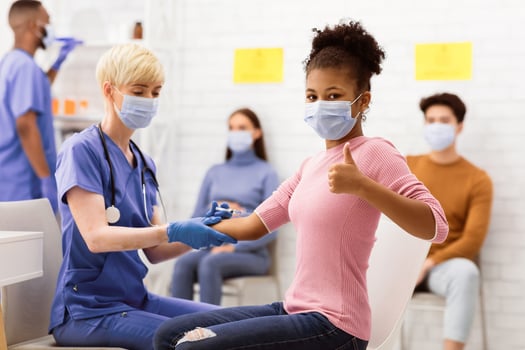 Successful Coronavirus Vaccination. Happy Vaccinated Black Teen Girl Gesturing Thumbs Up After Covid-19 Vaccine Injection In Hospital. Corona Virus Protection And Immunization. Selective Focus photo
