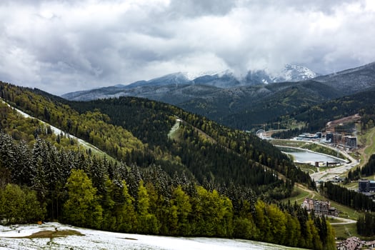 Stunning mountain landscape showcases a forest, lake, snowy peaks under a cloudy sky. A scenic view captures the breathtaking panorama of mountains, lush green forests, and a serene lake under skies photo