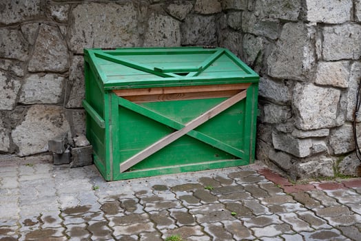 Green wooden crate against stone wall on paved ground. photo
