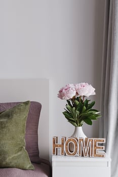 Cozy Home Concept. Pastel Pink Peony Flowers in a White Ceramic Vase and Home Sign on a Bedside Table photo