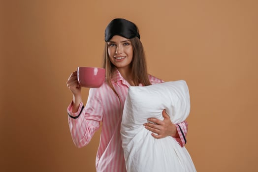 Conception of sleep products... With cup and pillow. Young pretty woman is against background in the studio photo