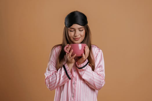 Pink ,pajama, with ,,cup of drink. Young pretty woman is against background in the studio photo