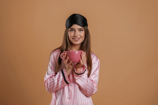 Pink pajama, with ,cup ,,of drink. Young pretty woman is against background in the studio photo