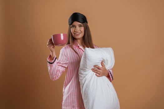 Conception of sleep products.. With cup and pillow. Young pretty woman is against background in the studio photo